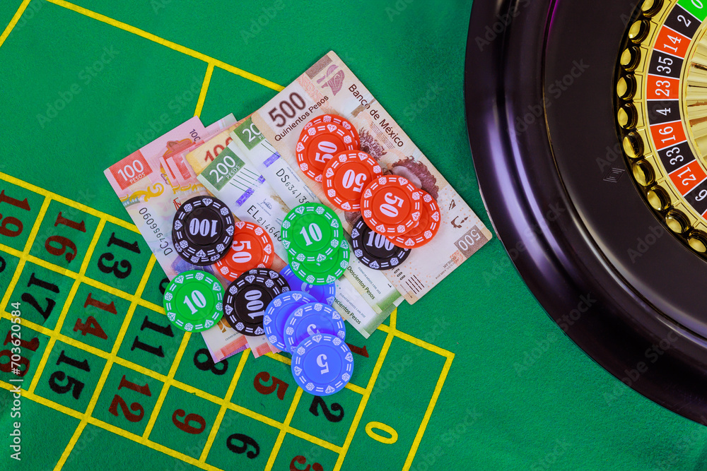 An casino roulette table with Mexican peso banknotes, poker chips is displayed on green gaming surface